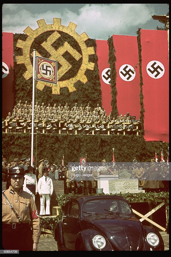 上图：1938年6月25日，希特勒在沃尔夫斯堡参加大众汽车厂的奠基仪式，前面是一辆大众甲壳虫汽车。希特勒上台后不久，就要求生产一种普通德国人买得起的「人民汽车」，可容纳2名成人和3名儿童、最高时速可达100km/h、最好采用风冷发动机，只卖990马克。奥地利工程师费迪南德·保时捷根据这一要求设计出著名的大众甲壳虫汽车。1936年10月12日，三辆大众VW-1下线。1938年，大众汽车公司在沃尔夫斯堡建厂，计划年产150万辆。二战期间，大众的生产能力被用于军备生产。