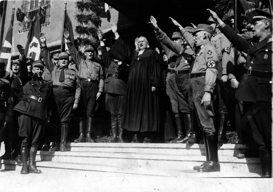 上图：1933年9月，路德维希·穆勒（Ludwig Müller）在威登堡召开的德国全国宗教大会上行纳粹礼。穆勒毕业于敬虔主义福音派高中，在哈勒大学（Halle）学习神学，一战时担任海军随军牧师，1931年加入纳粹党。1933年1月希特勒上台之后，德意志基督徒（German Christians）在德意志福音教会联合会（German Evangelical Church Confederation）的一些成员教会中掌权，同年4月将改组织改名为德意志福音教会（German Evangelical Church），成为受纳粹党领导的帝国教会（Protestant Reich Church）。同年9月，穆勒被选为帝国主教。从此德意志福音教会成为纳粹的跟班，战后被解散，由德国福音教会（Evangelical Church in Germany）取代。